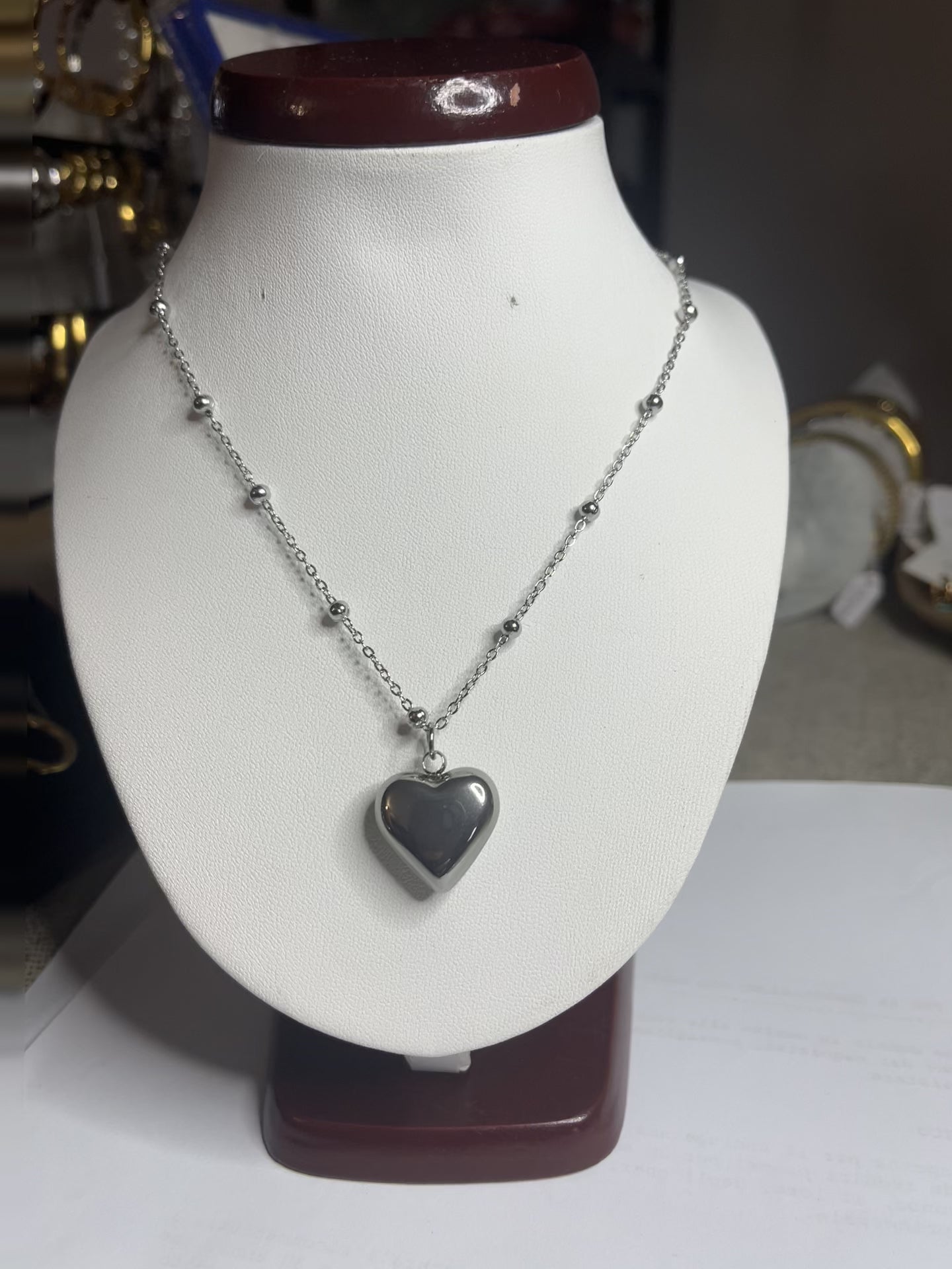 Collana Allegra in acciaio premium con catena decorata da sfere e ciondolo cuore, variante placcato argento, esposta su busto espositore bianco