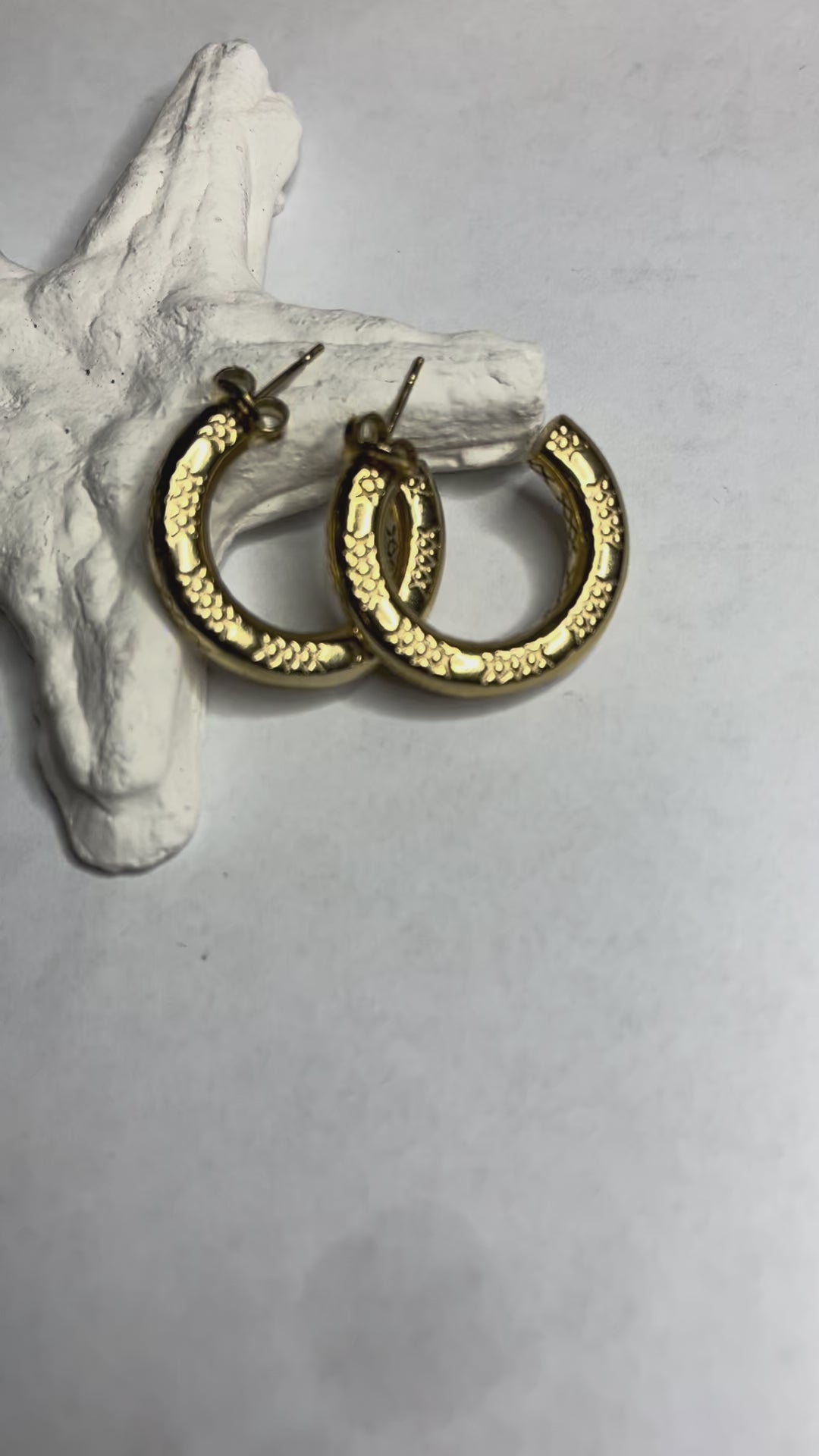 Orecchini a cerchio placcati oro con texture decorativa tridimensionale, appoggiati su corallo bianco