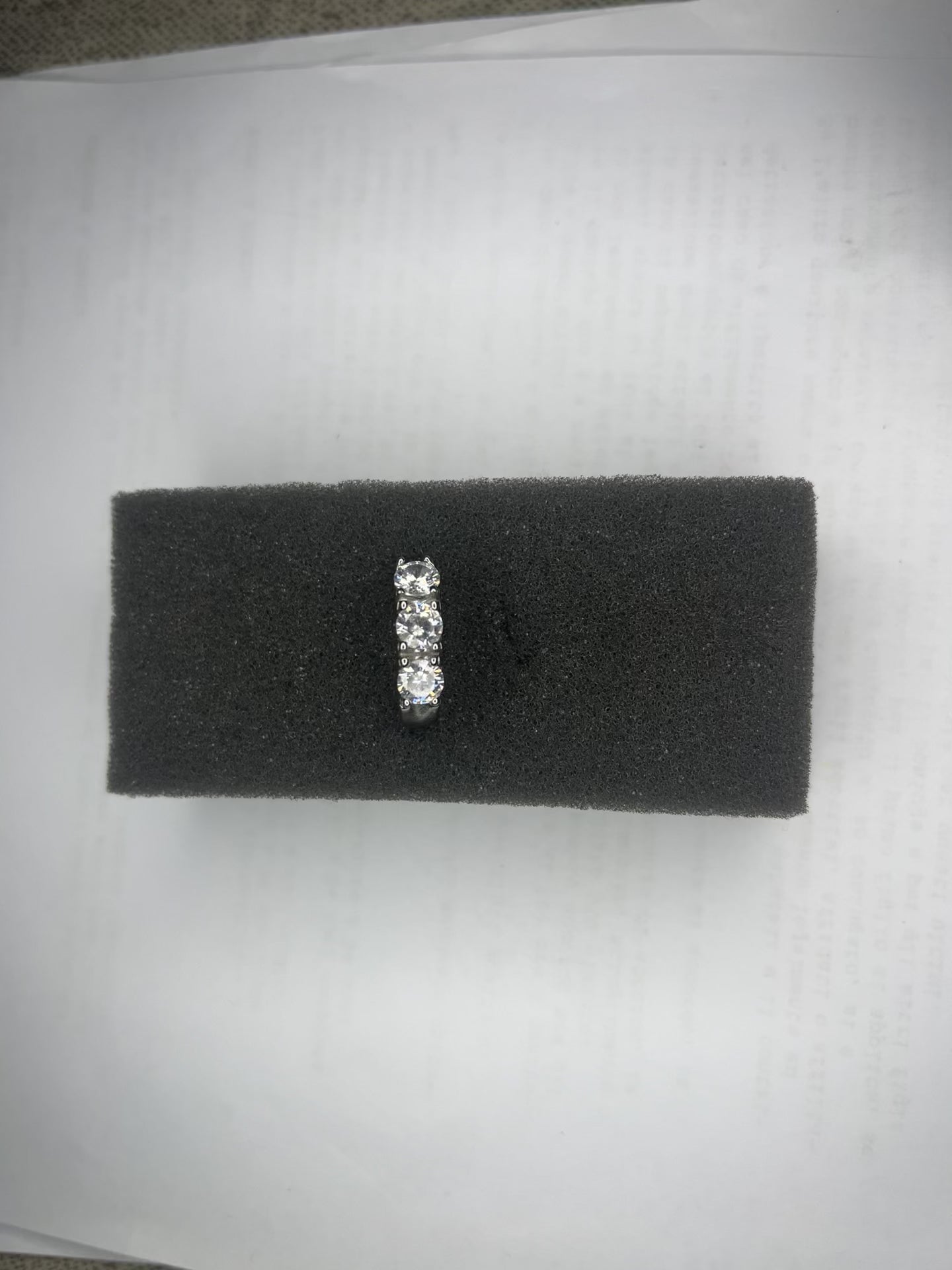 Anello Trio in acciaio premium placcato argento con tre zirconi brillanti perfettamente incastonati, fotografato su superficie scura che esalta la brillantezza delle pietre