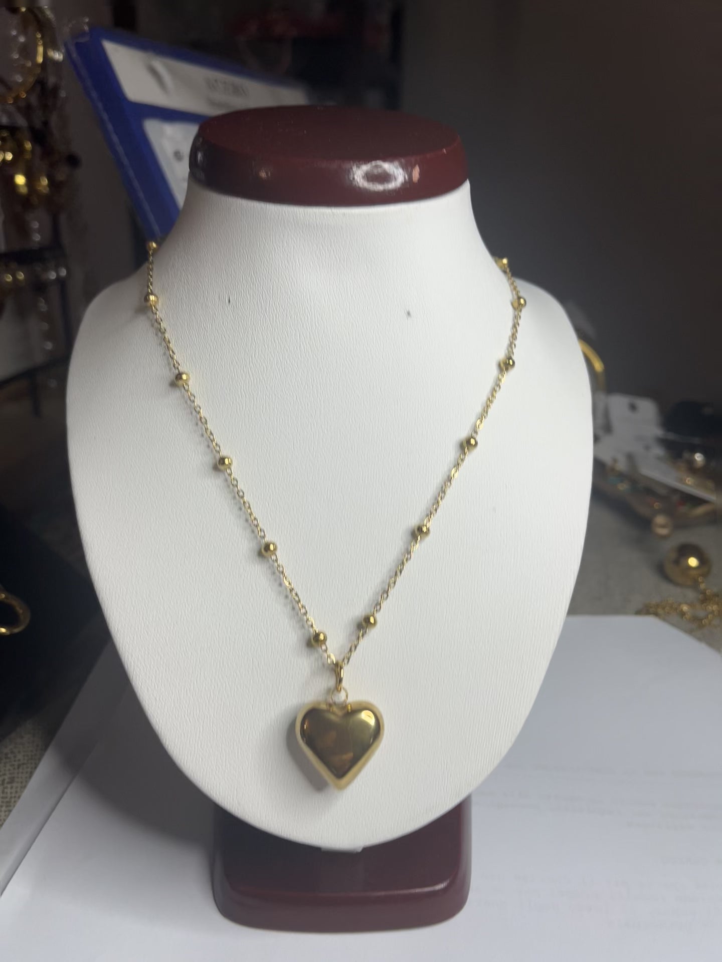 Collana Allegra in acciaio premium con catena decorata da sfere e ciondolo cuore, variante placcato oro, esposta su busto espositore bianco