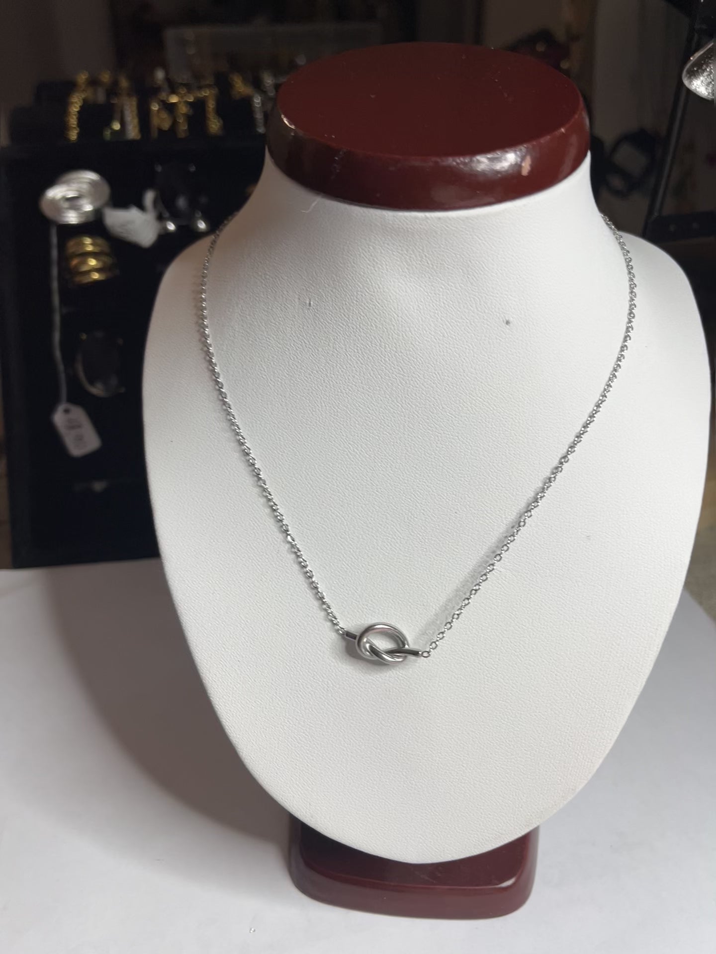 Collana Love Knot con pendente a nodo intrecciato dorato su catena delicata, simbolo di amore eterno esposto su busto bianco