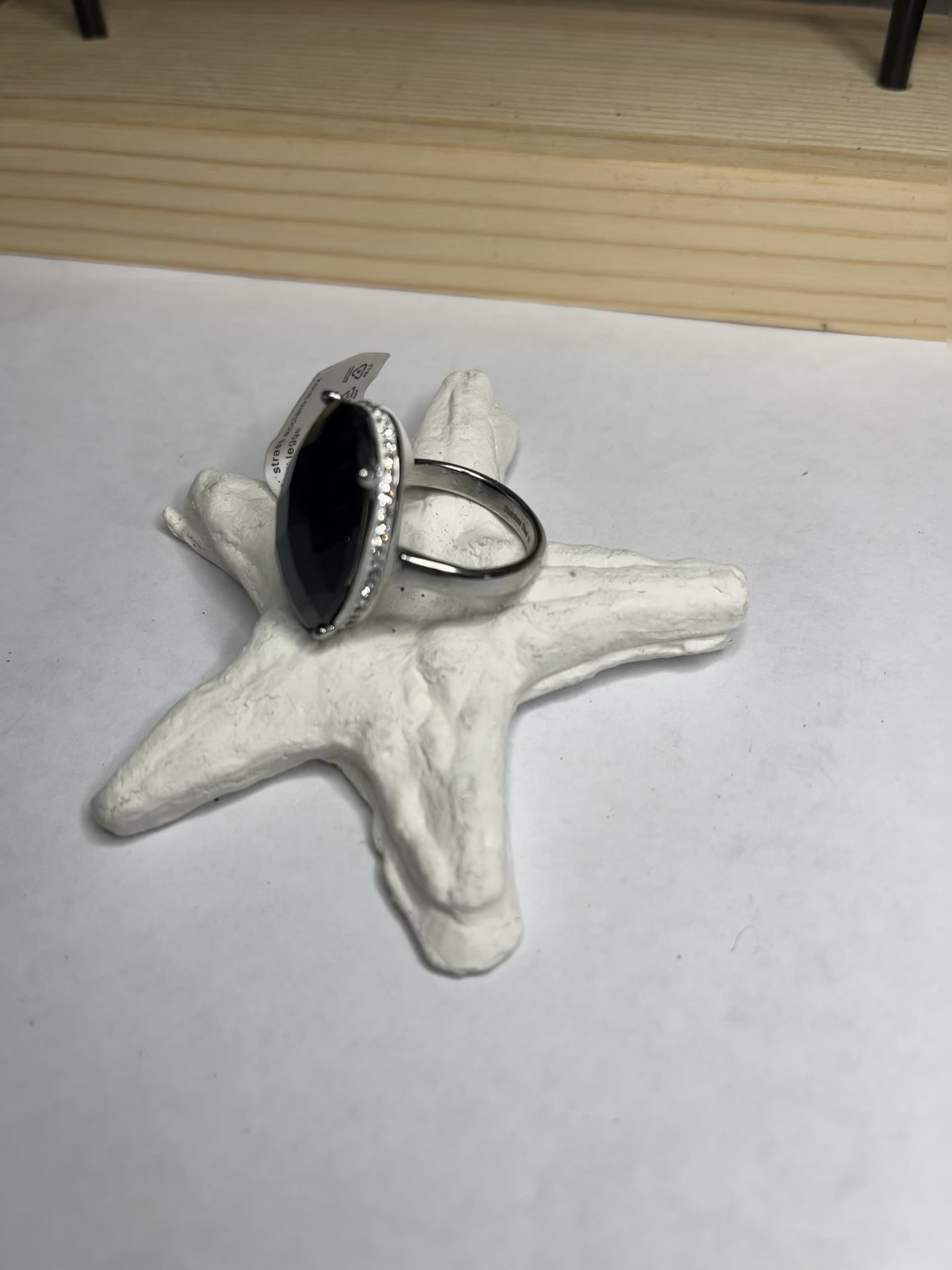 Anello con pietra nera ovale lucida e montatura argentata o dorata decorata, appoggiato su stella marina bianca