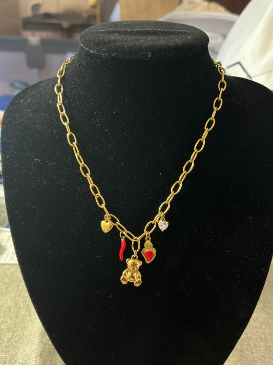 Rita - Collana placcata oro con catena e ciondoli portafortuna tra cui orsetto, cornetto rosso e cuori, esposta su busto nero