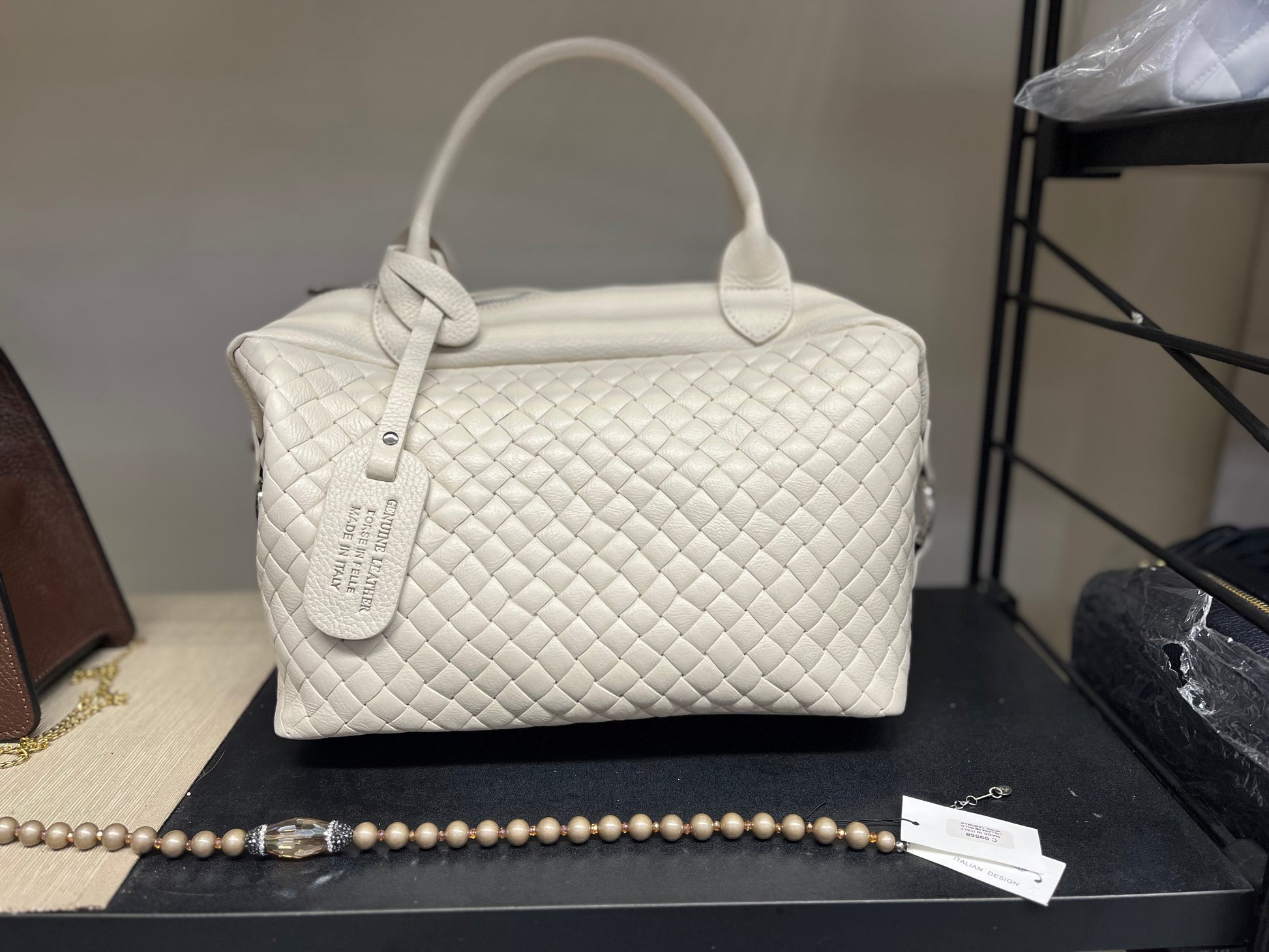 Victoria - Borsa trapuntata elegante in pelle beige con manici e tag identificativo, design a rombi e finitura lucida, esposta con bracciale di perle