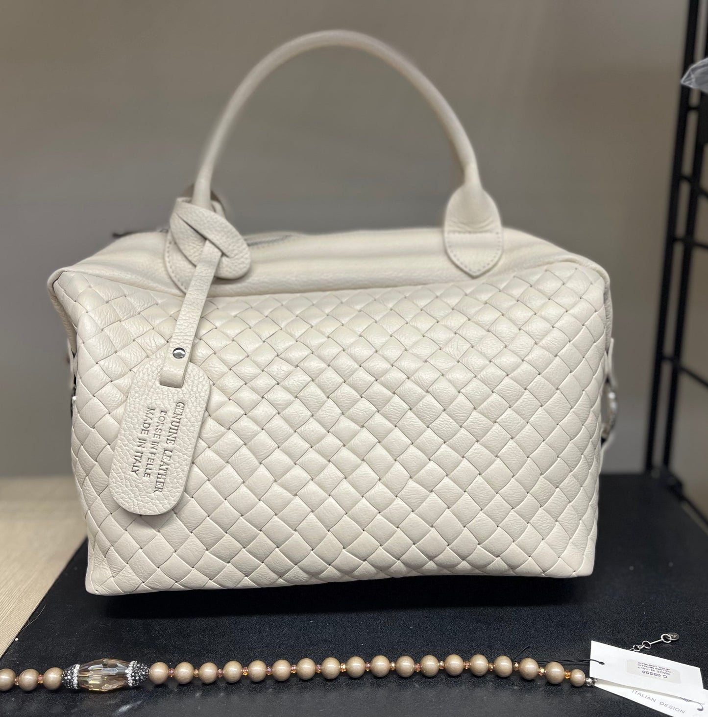 Victoria - Borsa trapuntata elegante in pelle beige con manici e tag identificativo, design a rombi e finitura lucida, esposta con bracciale di perle