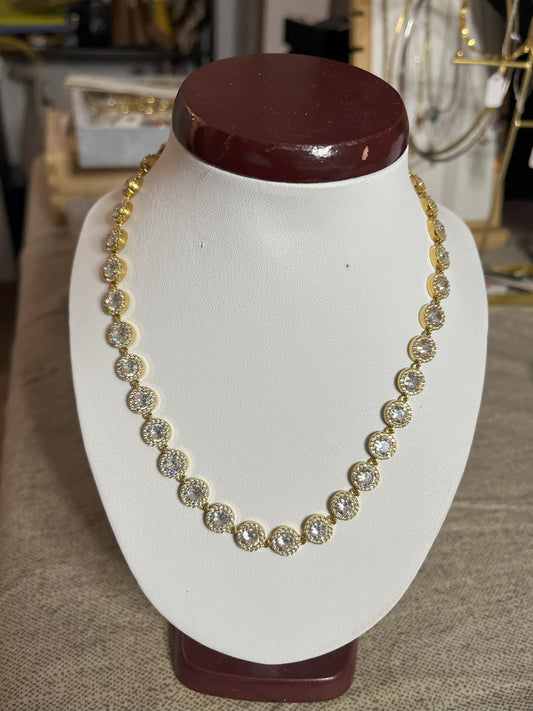 Collana Dorata Infinity Shines con elementi circolari dorati luminosi placcati oro su espositore bianco, simbolo di eternità e infinito per donna