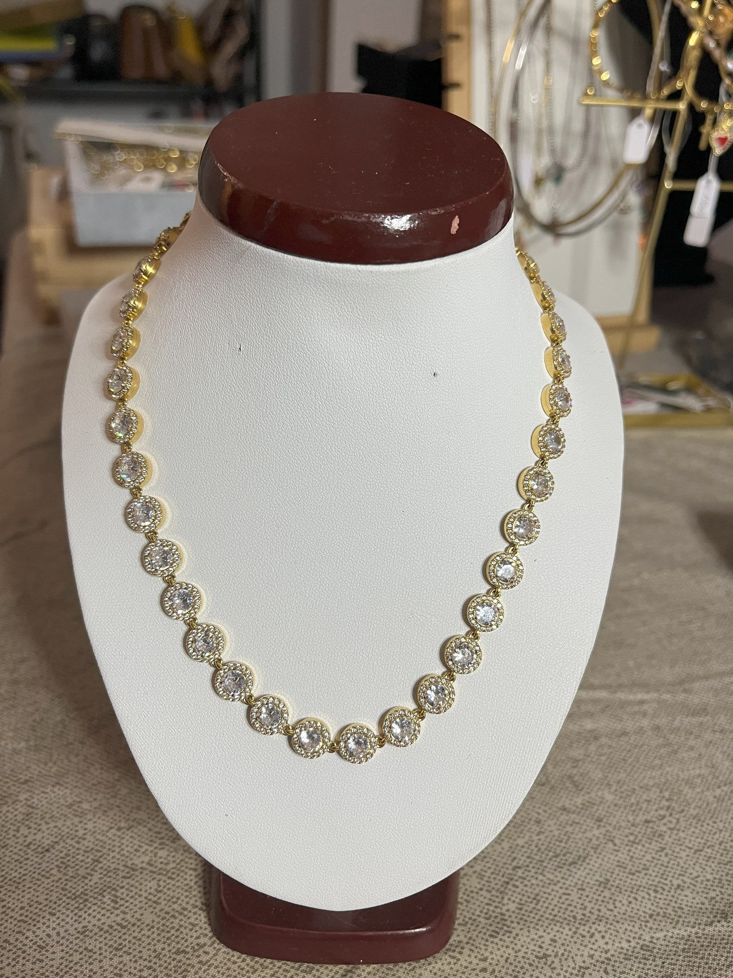 Collana Dorata Infinity Shines con elementi circolari dorati luminosi placcati oro su espositore bianco, simbolo di eternità e infinito per donna