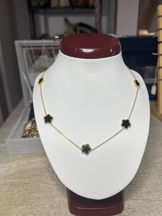 Collana Élégance Suprême in ottone dorato con cinque elementi floreali neri disposti simmetricamente, esposta su busto bianco, design elegante e raffinato stile italiano