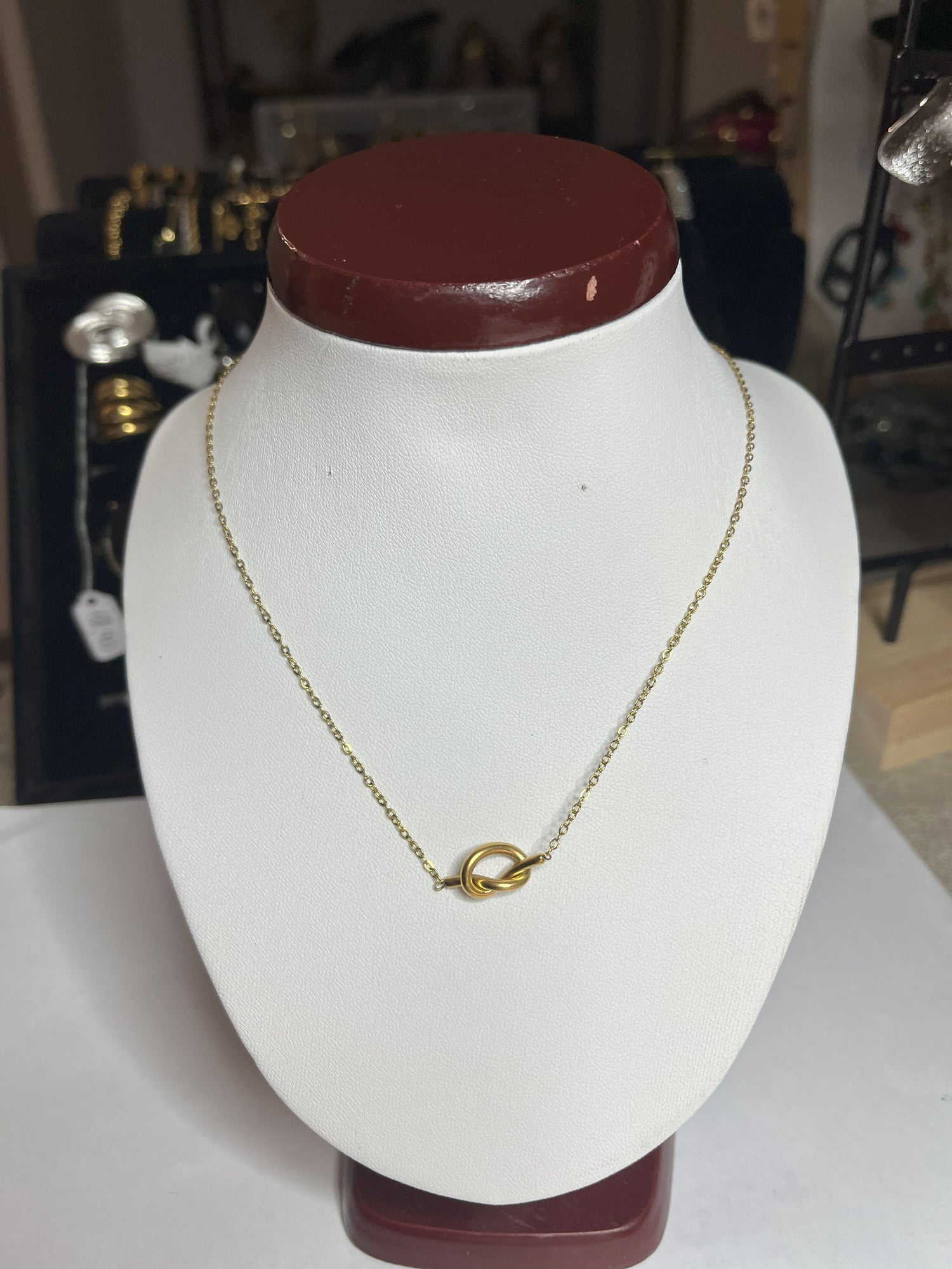 Collana Love Knot con pendente a nodo intrecciato dorato su catena delicata, simbolo di amore eterno esposto su busto bianco