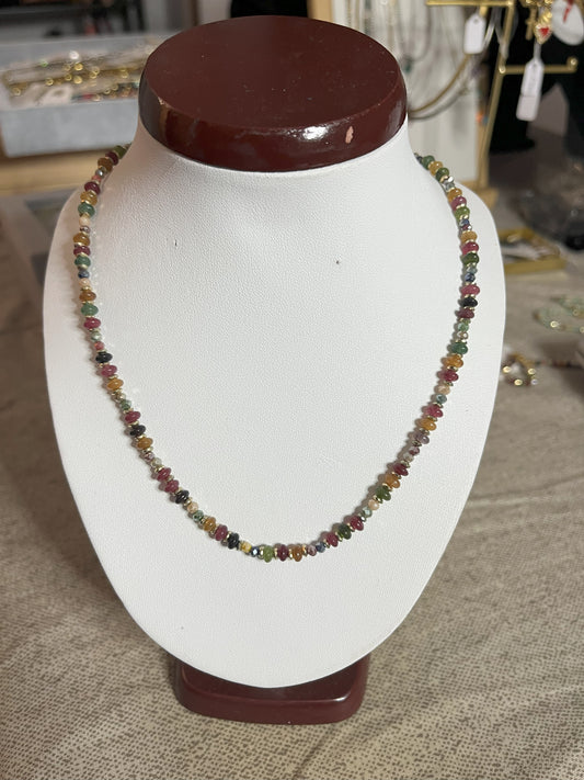 Collana Mosaico Prezioso disponibile in due varianti: multicolore con pietre rosse, verdi, blu e oro, e verde-oro con tonalità smeraldo e dorate, su espositore bianco