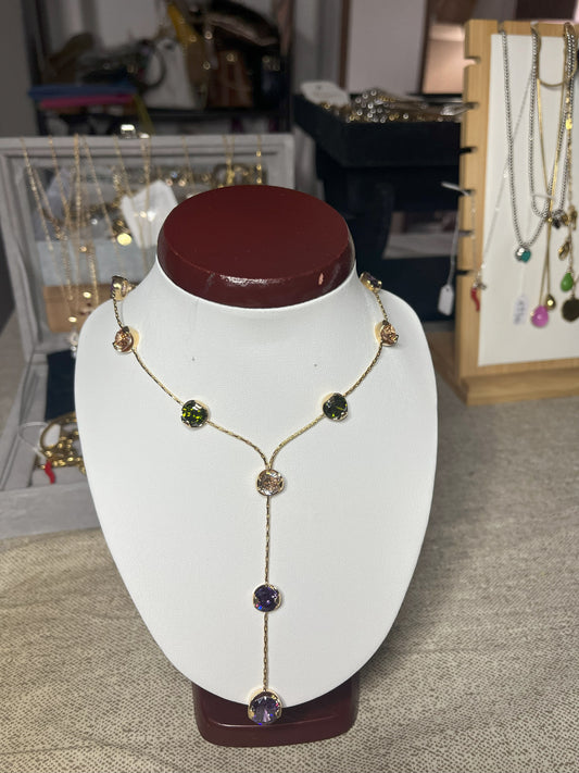 Collana Ottone e Cristalli Bohémien esposta su busto bianco, design asimmetrico con pendente lungo, cristalli verdi e viola incastonati in ottone dorato, stile bohémien elegante