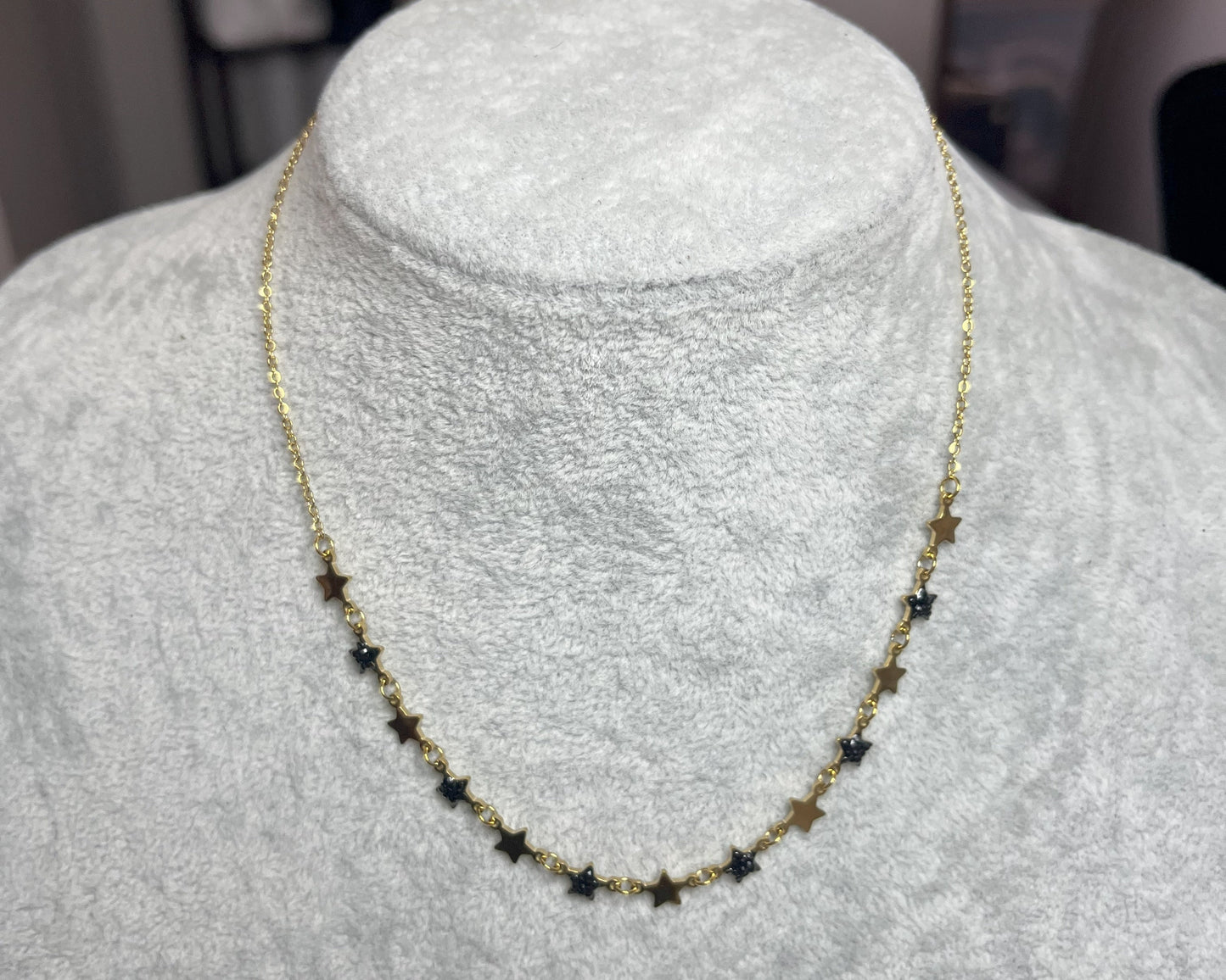 Collana Stelline Dorate - elegante catena dorata con piccole stelle nere alternate, gioiello minimalista su busto espositore