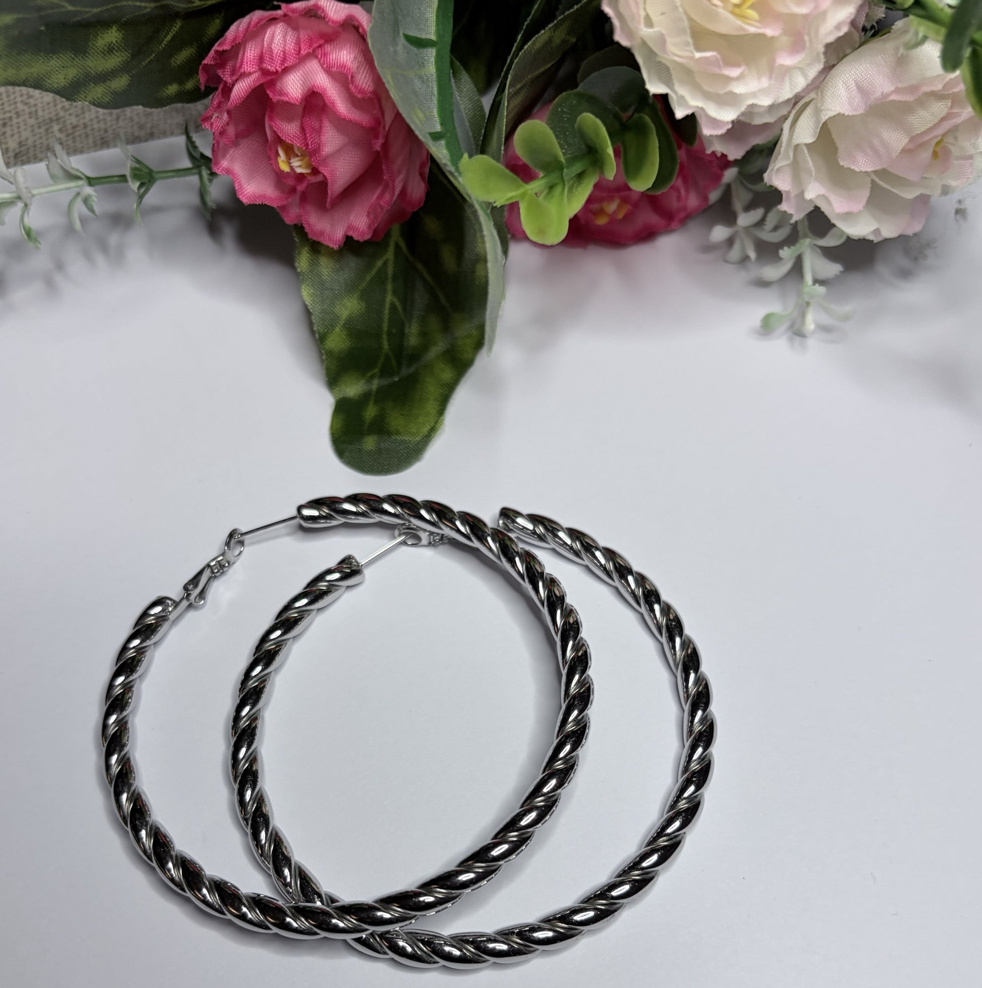 Orecchini cerchio twist intrecciato placcati argento — vista dall'alto su sfondo bianco con fiori