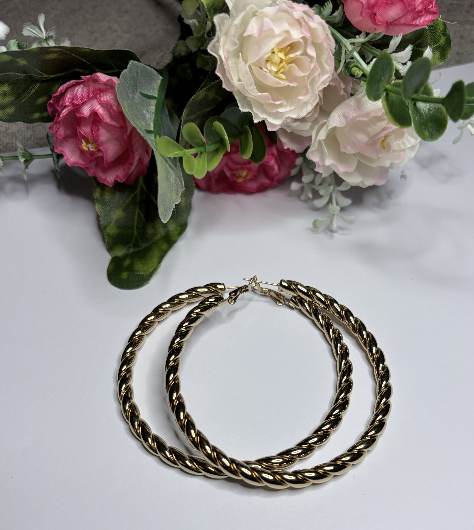 Orecchini cerchio twist placcati oro — vista laterale su sfondo bianco con fiori