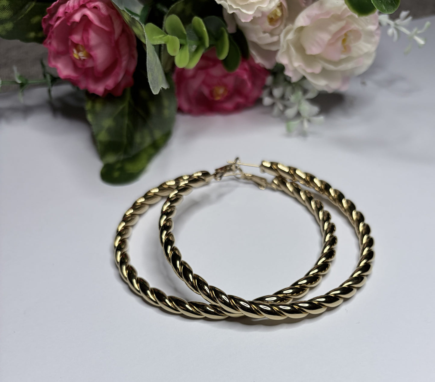 Orecchini cerchio twist placcati oro — vista laterale su sfondo bianco con fiori