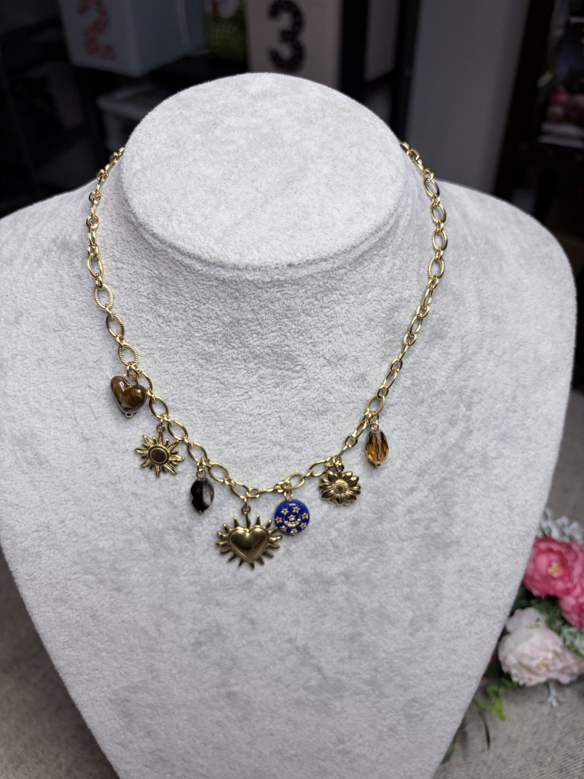 Collana dorata con 7 charm vista frontale su busto bianco: sacro cuore, sole, girasole, cristalli.