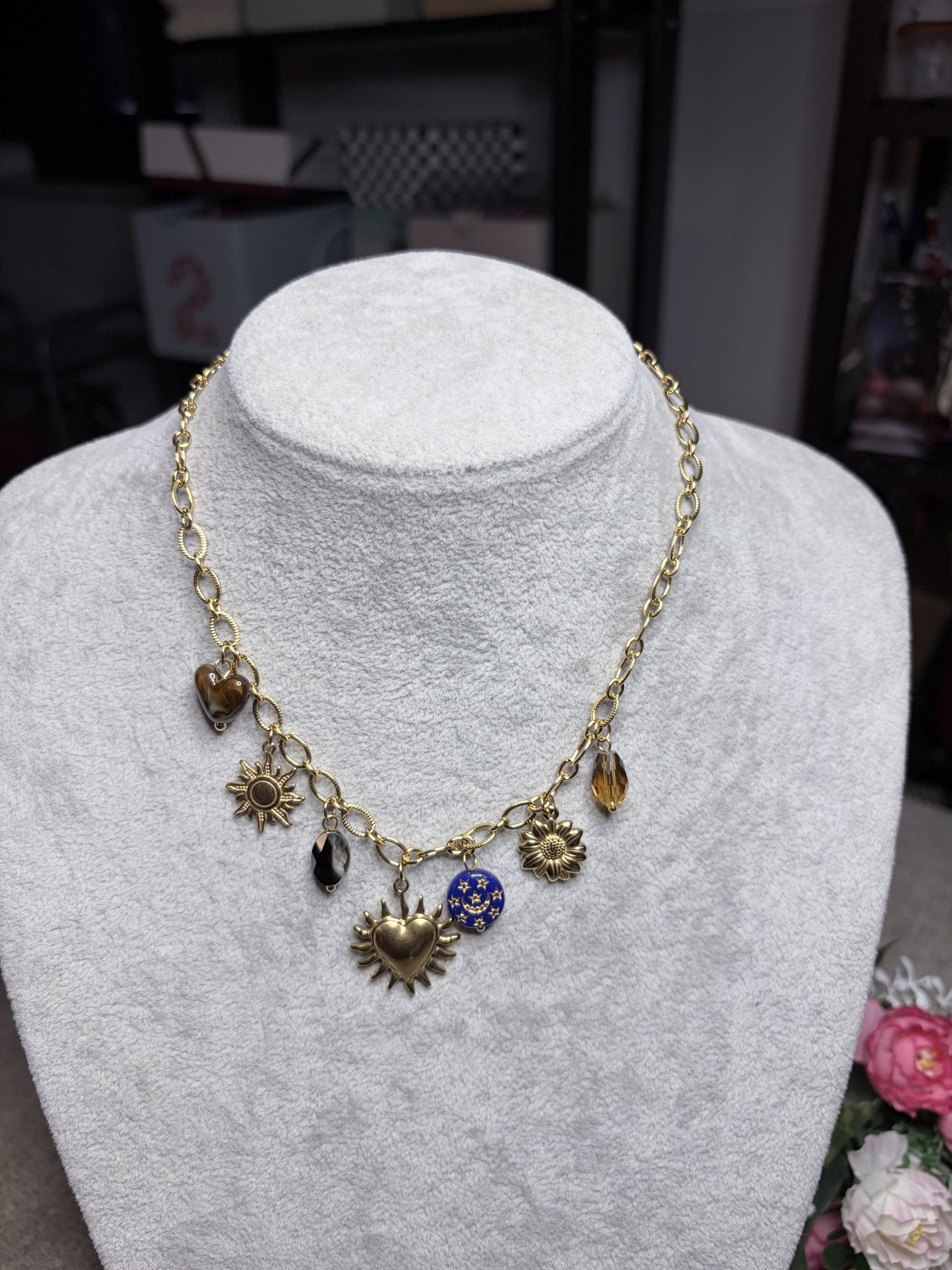 Collana dorata con 7 charm vista frontale su busto bianco: sacro cuore, sole, girasole, cristalli