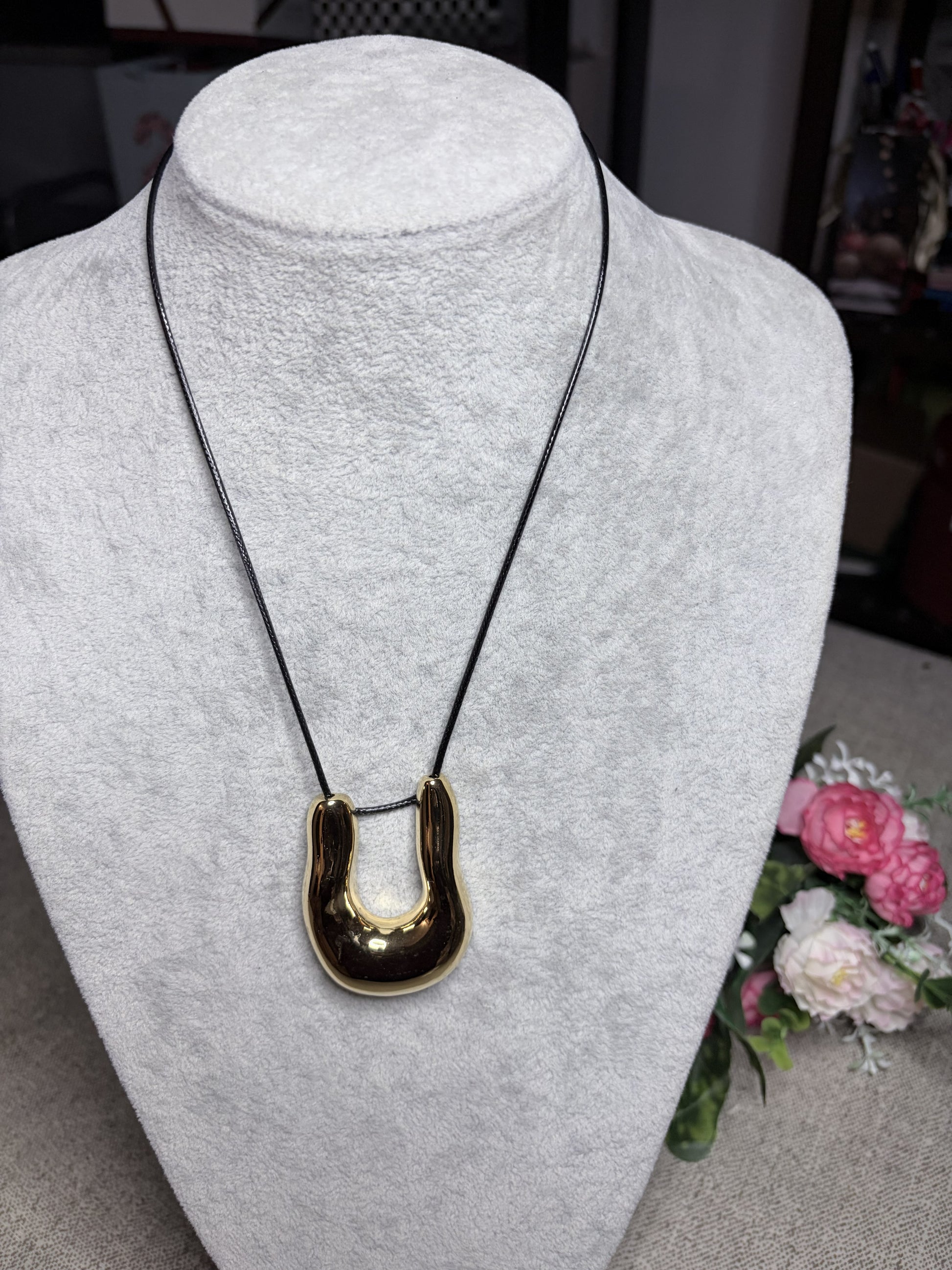 Collana cordino pelle nera con ciondolo ferro di cavallo dorato su busto bianco — vista frontale