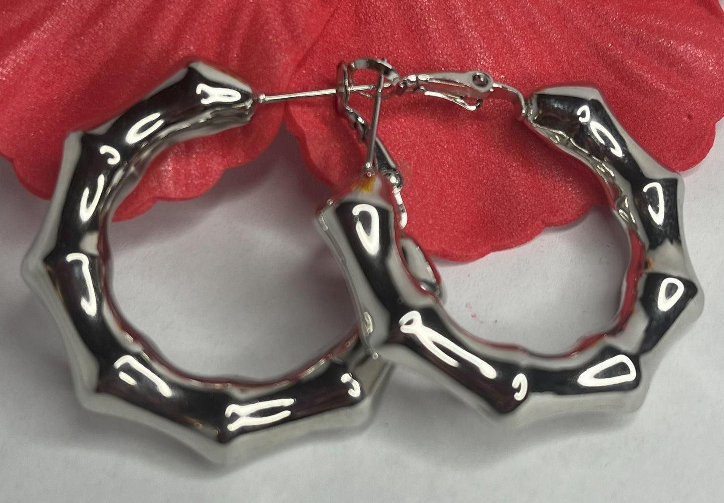 Orecchini Bambù Prezioso placcati argento con texture bambù a cerchio, design naturale elegante su sfondo bianco con fiore rosso decorativo