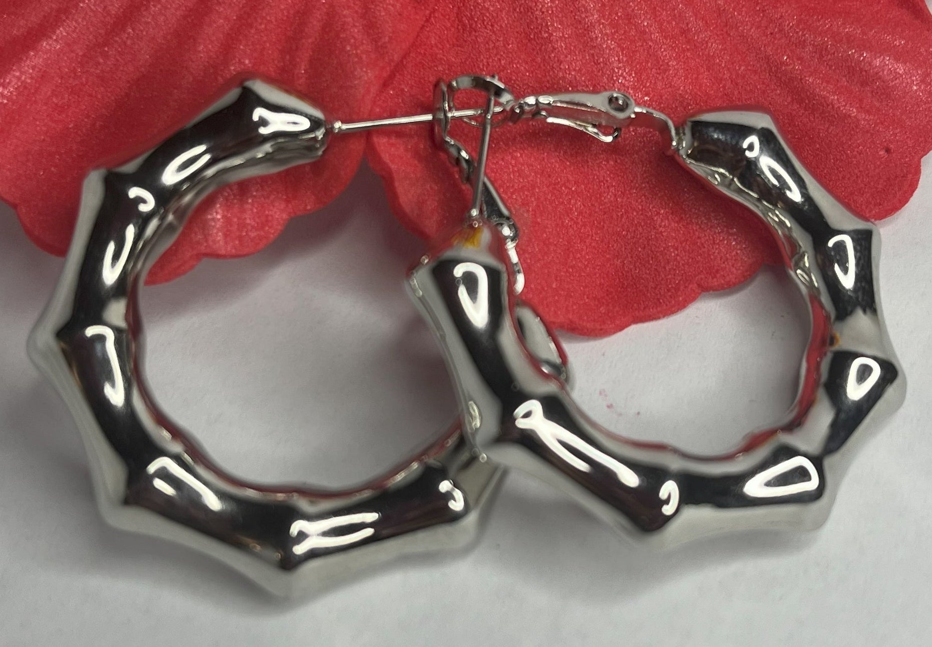 Orecchini Bambù Prezioso placcati argento con texture bambù a cerchio, design naturale elegante su sfondo bianco con fiore rosso decorativo