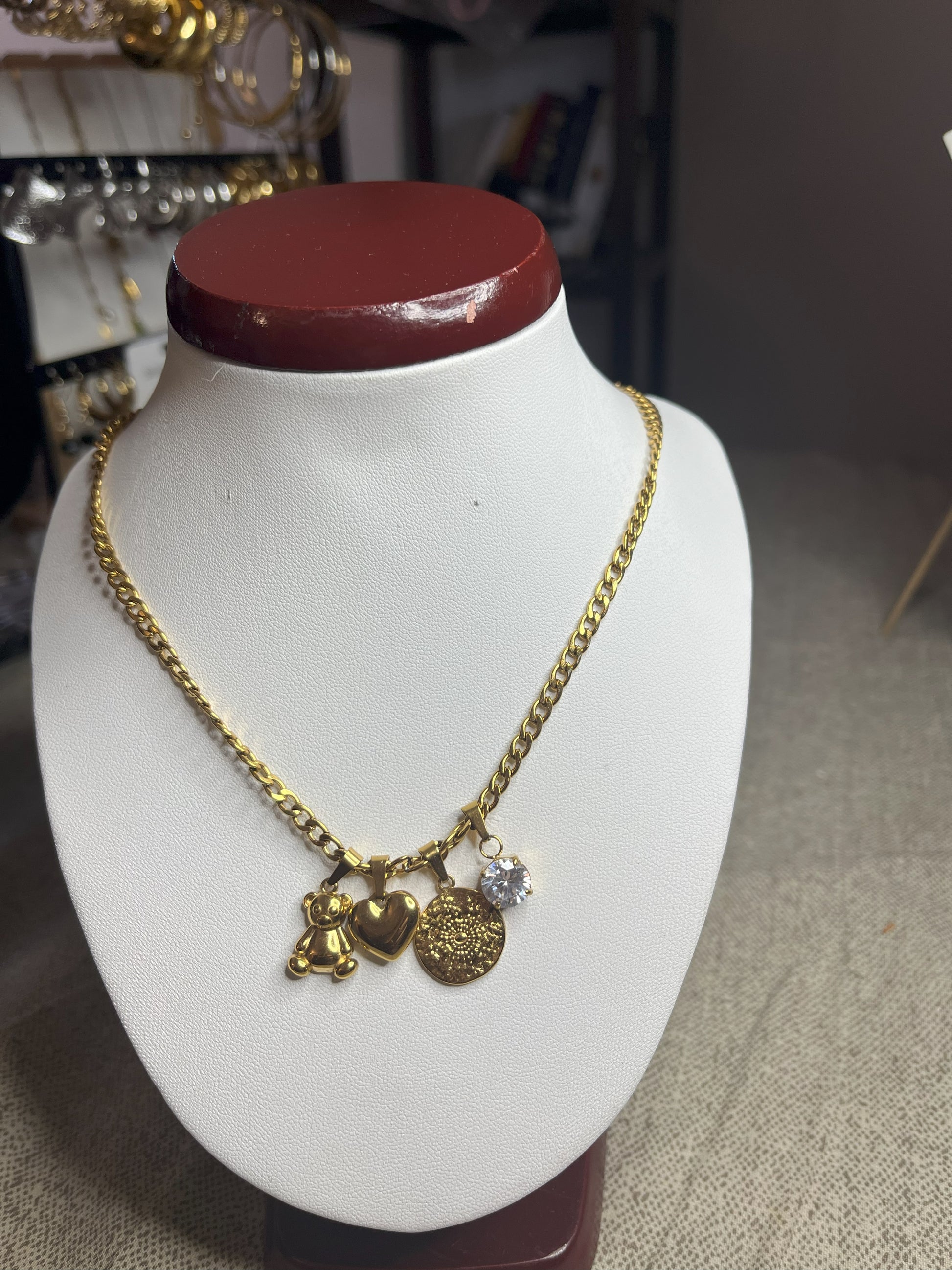 Collana Tesori Dorati in acciaio premium dorato con charm removibili: orsetto, cuore, medaglia decorativa e cristallo brillante su catena elegante. La collana è su espositore bianco