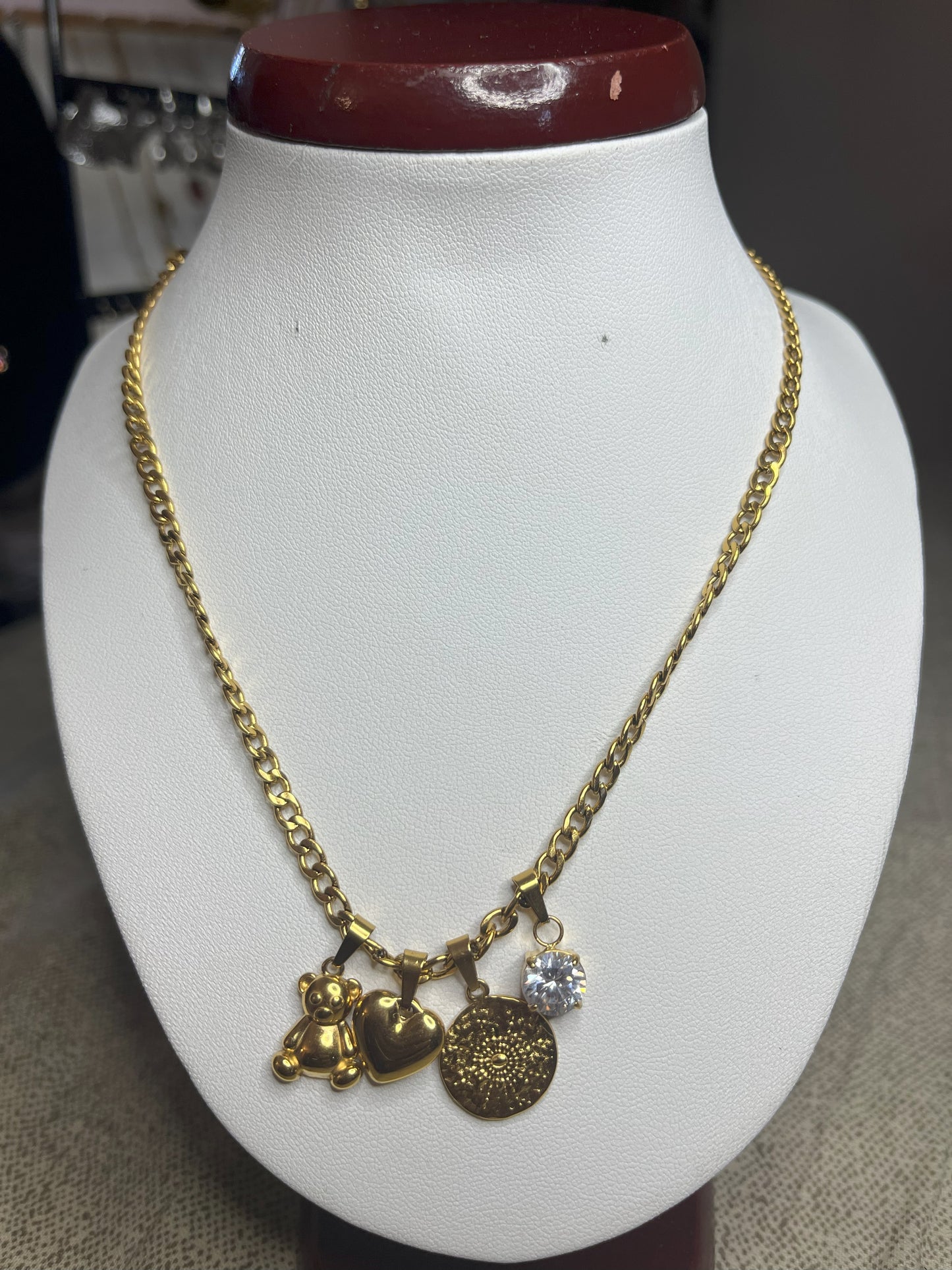 Collana Tesori Dorati in acciaio premium dorato con charm removibili: orsetto, cuore, medaglia decorativa e cristallo brillante su catena elegante. La collana è su espositore bianco