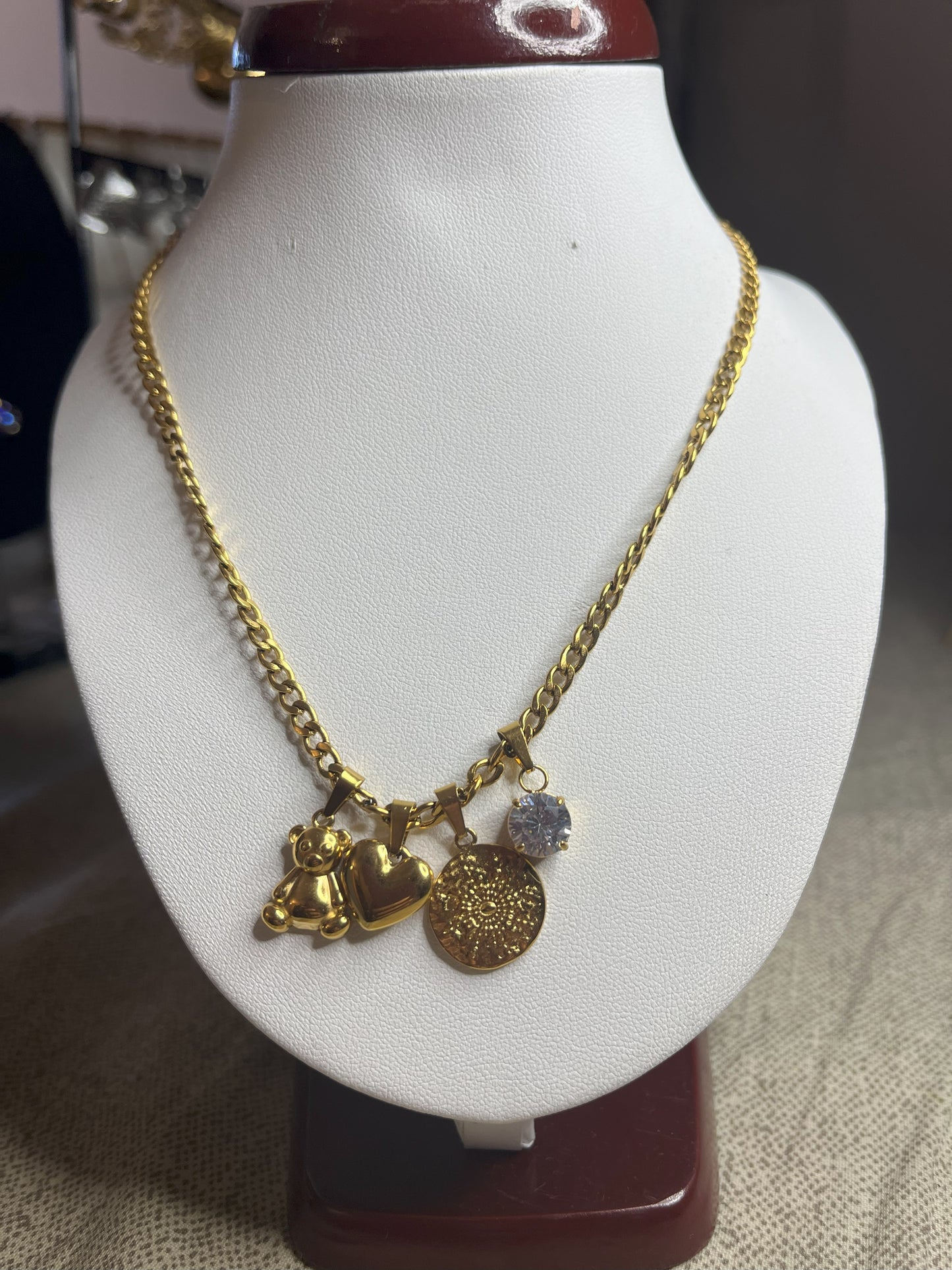 Collana Tesori Dorati in acciaio premium dorato con charm removibili: orsetto, cuore, medaglia decorativa e cristallo brillante su catena elegante. La collana è su espositore bianco