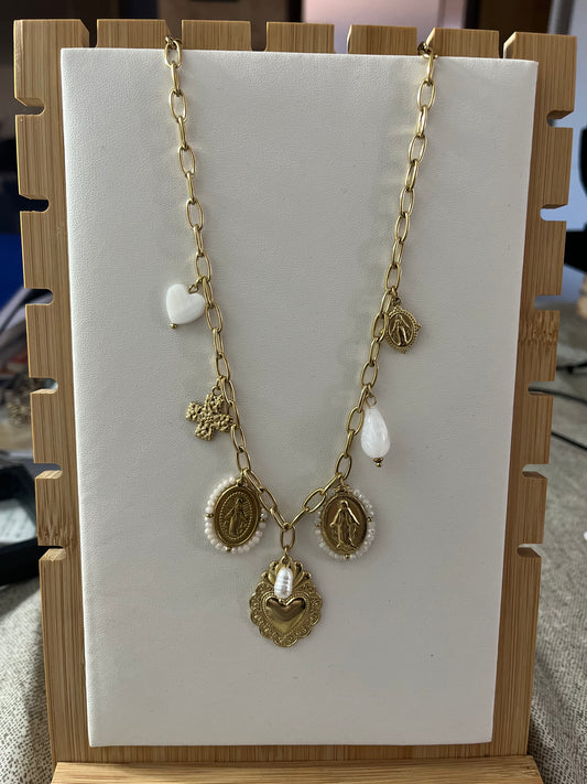 Collana Marzia lunga dorata con ciondoli vintage esposta su supporto in legno, featuring pendente centrale a cuore e decorazioni ornate in stile classico