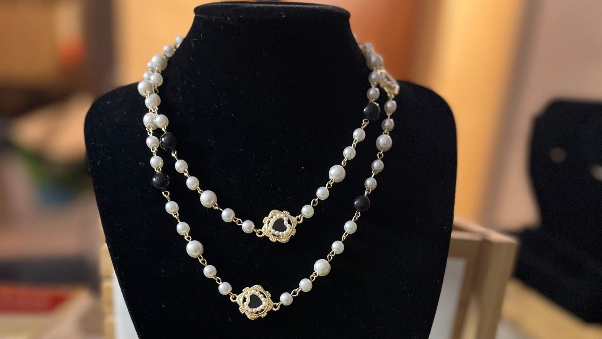 Collana di perle bianche con tre ciondoli a forma di cuore sacro dorati esposta su busto nero
