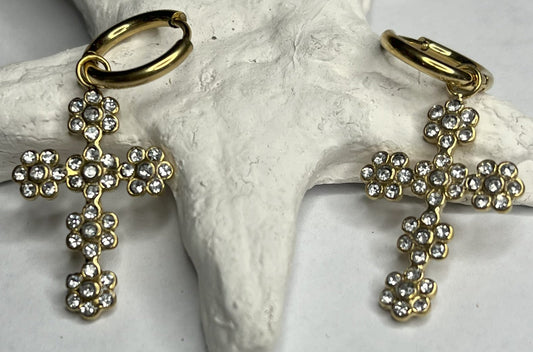 Orecchini pendenti con ciondoli a croce decorati con cristalli diamantati e ganci dorati, appoggiati su stella marina bianca