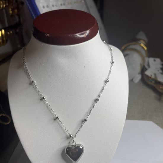  Collana Allegra in acciaio premium con catena decorata da sfere e ciondolo cuore, variante placcato argento, esposta su busto espositore bianco 