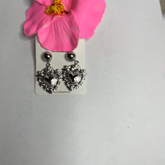Orecchini dorati a forma di sacro cuore con dettagli intarsiati e lavorazione artigianale su sfondo con fiore rosa