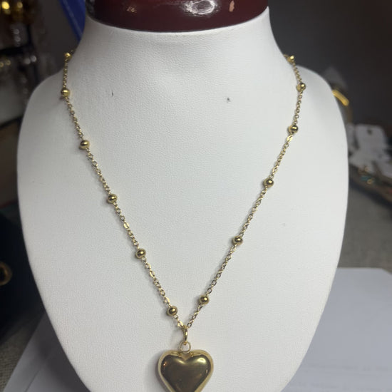  Collana Allegra in acciaio premium con catena decorata da sfere e ciondolo cuore, variante placcato oro, esposta su busto espositore bianco 