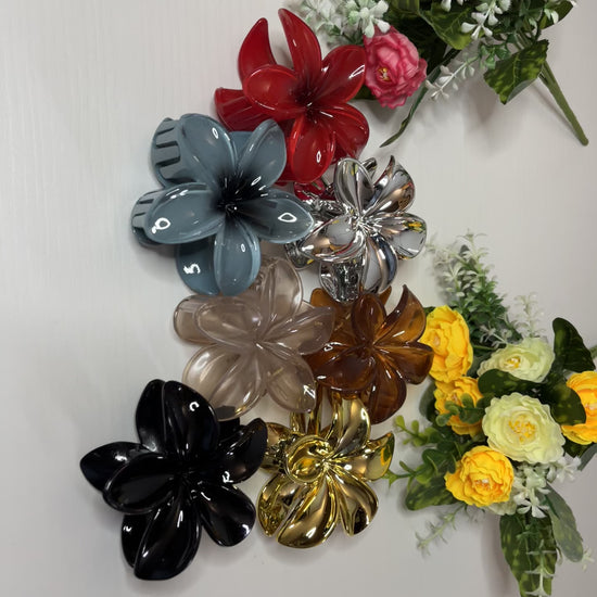 Elegante pinza hawaiana per capelli a forma di fiore con petali lucidi, posizionata accanto a un bouquet di fiori freschi gialli e bianchi