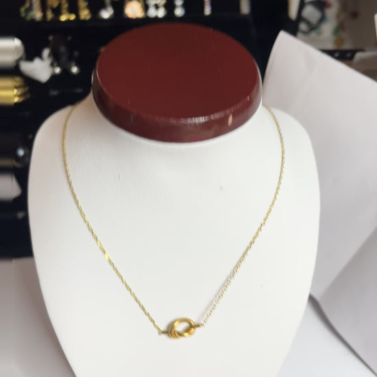 Collana Love Knot con pendente a nodo intrecciato dorato su catena delicata, simbolo di amore eterno esposto su busto bianco