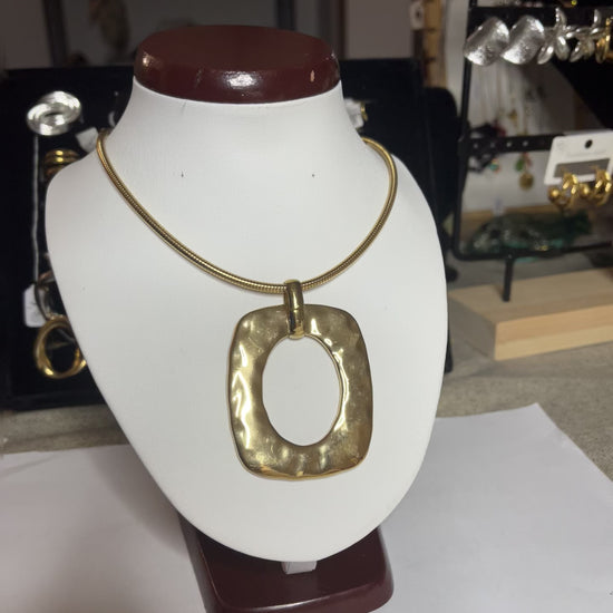 Collana Charlize in acciaio inossidabile placcato oro con catena a maglia serpente e pendente geometrico quadrato, esposta su busto bianco