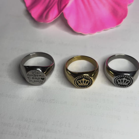 Anello Regina Mamy in acciaio premium placcato argento con incisione dedicata alla maternità, fotografato su superficie bianca con fiore rosa
