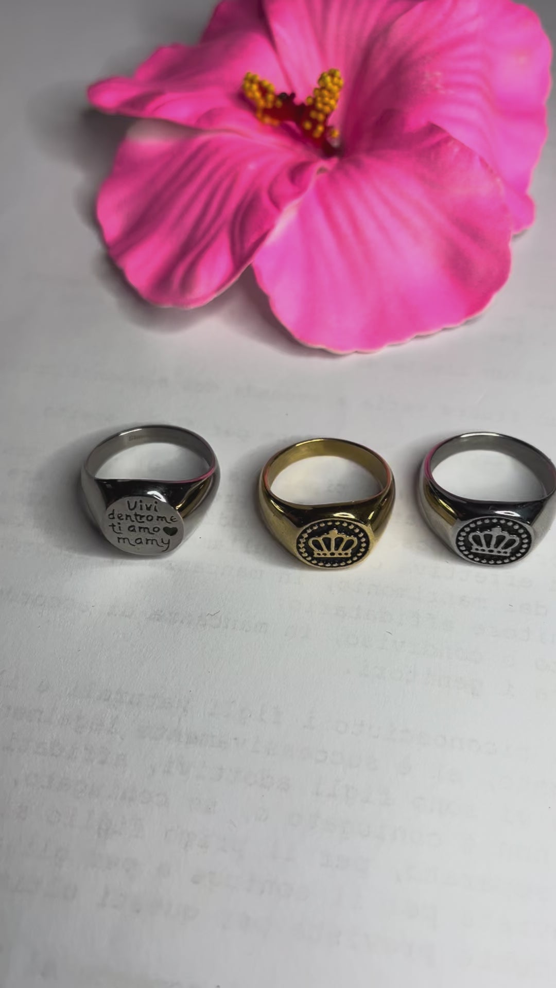 Anello Regina Mamy in acciaio premium placcato argento con incisione dedicata alla maternità, fotografato su superficie bianca con fiore rosa