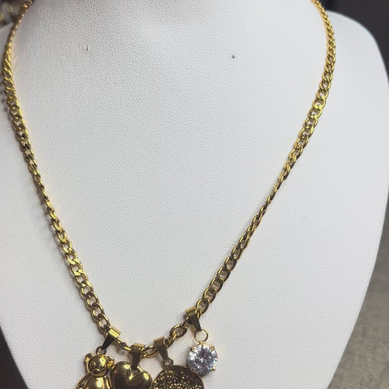 Collana Tesori Dorati in acciaio premium dorato con charm removibili: orsetto, cuore, medaglia decorativa e cristallo brillante su catena elegante. La collana è su espositore bianco