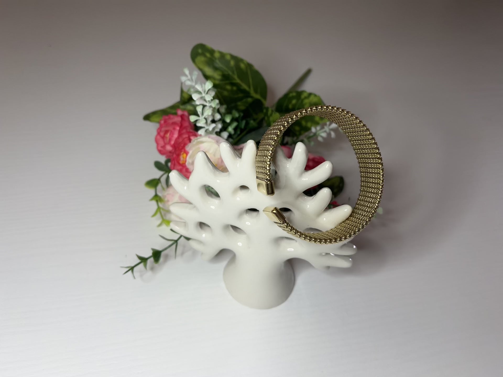 Braccialetto Cocò-G con elegante maglia dorata mesh e chiusura magnetica, esposto con decorazioni floreali rosa