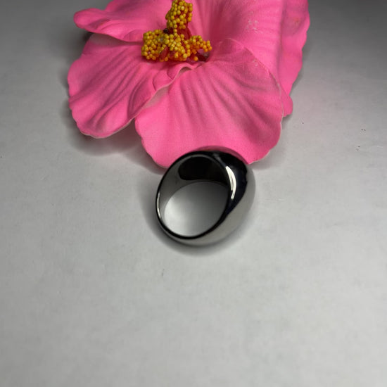 Anello Riflesso Argento in acciaio inossidabile con finitura a specchio lucida, design ovale elegante, fotografato su petalo di fiore rosa che ne esalta la brillantezza