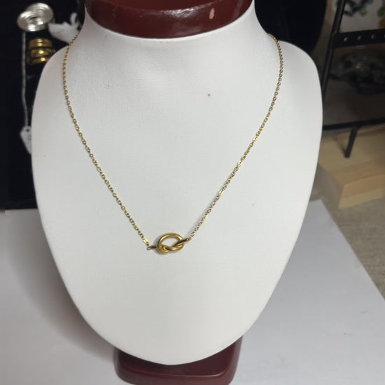 Collana Love Knot con pendente a nodo intrecciato dorato su catena delicata, simbolo di amore eterno esposto su busto bianco