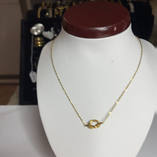 Collana Love Knot con pendente a nodo intrecciato dorato su catena delicata, simbolo di amore eterno esposto su busto bianco