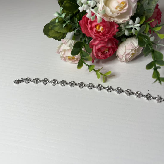  Braccialetto tennis placcato argento con quadrifogli portafortuna e cristalli scintillanti su sfondo bianco con foglie verdi