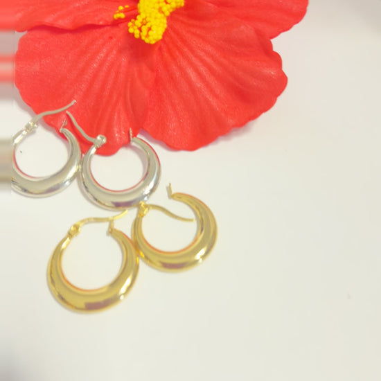 Set di orecchini creoli placcati, due paia in oro e argento, disposti su sfondo neutro con fiore rosso decorativo