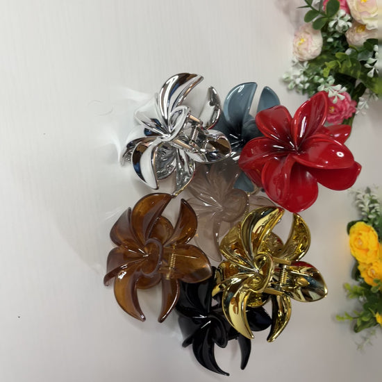Elegante pinza hawaiana per capelli a forma di fiore con petali lucidi, posizionata accanto a un bouquet di fiori freschi gialli e bianchi
