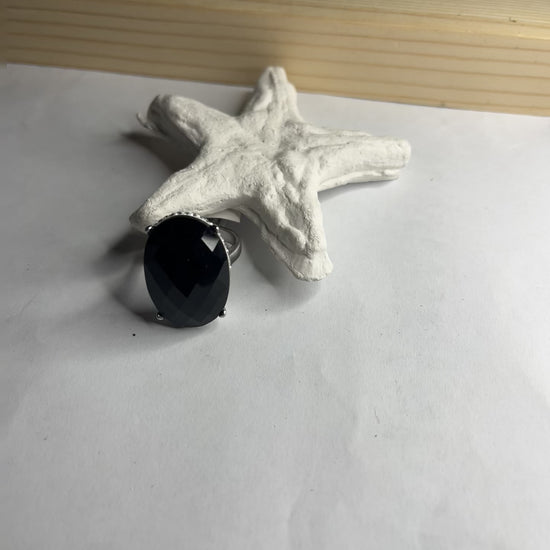  Anello con pietra nera ovale lucida e montatura argentata o dorata decorata, appoggiato su stella marina bianca