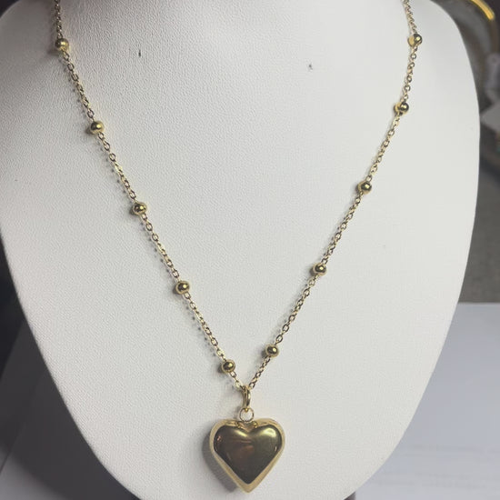  Collana Allegra in acciaio premium con catena decorata da sfere e ciondolo cuore, variante placcato oro, esposta su busto espositore bianco 