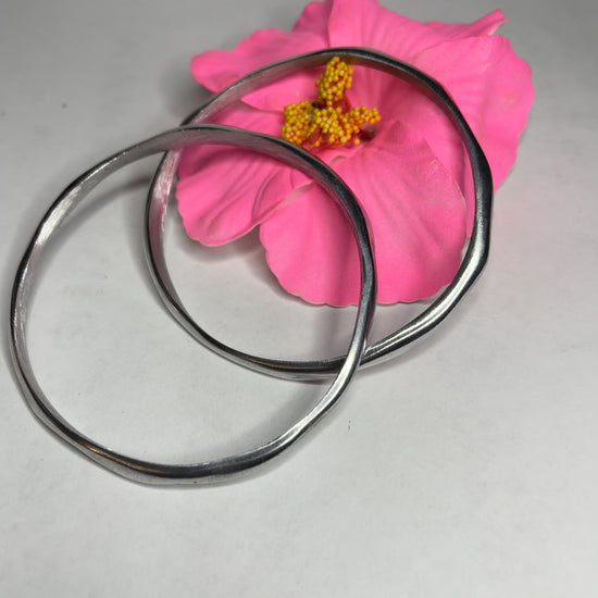 Braccialetto Rinascita in alluminio riciclato fatto a mano, design circolare minimalista con finitura lucida premium, fotografato accanto a un fiore rosa su sfondo neutro