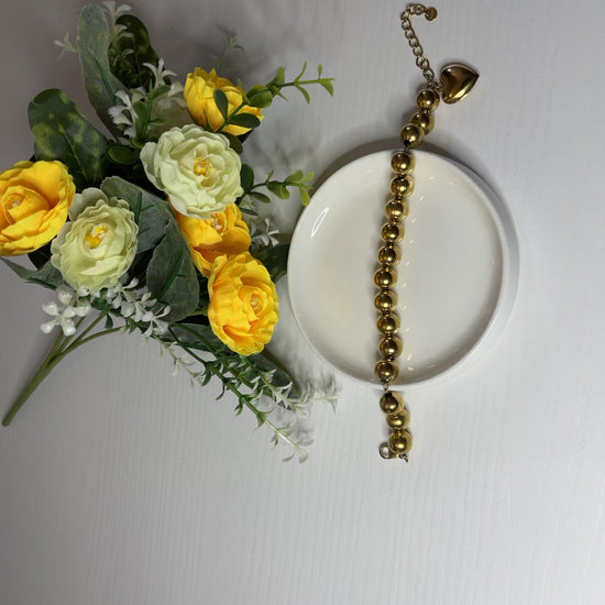Elegante braccialetto con sfere dorate lucide su fiori gialli e foglie verdi